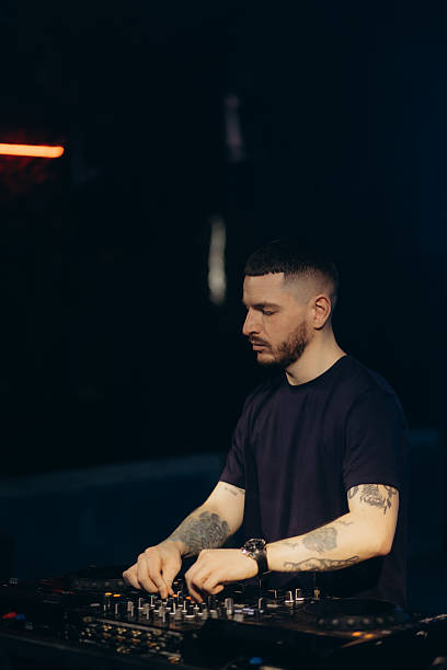 istock DJ Performing Live Set in Dark Club Environment with Concentrated Expression 2203380457