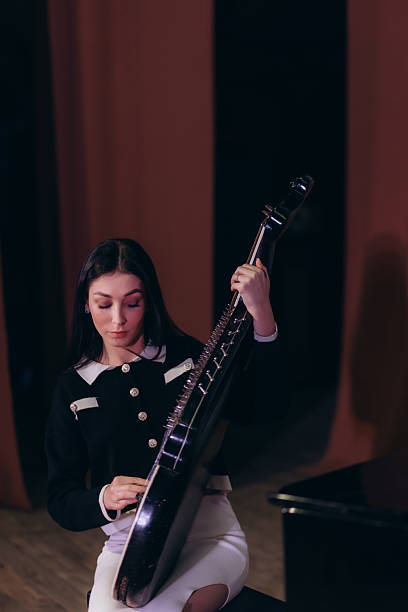 A woman in elegant attire performs with a stringed musical instrument on a stage, radiating concentration and grace, highlighting music, artistry, and passion for performing arts.