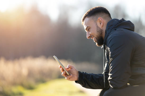 A handsome man with dark hair relaxing on bench and using smart phone.
