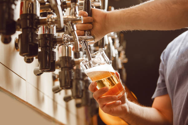 istock Faceless Bartender Pours Fresh Beer From Tap at Bustling Bar 2203387812