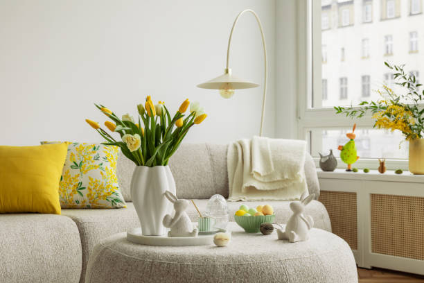 istock Bright living room with an Easter setup featuring yellow tulips in a white vase, soft textured pillows, and delicate decorations, creating a warm and festive ambiance. 2203387874