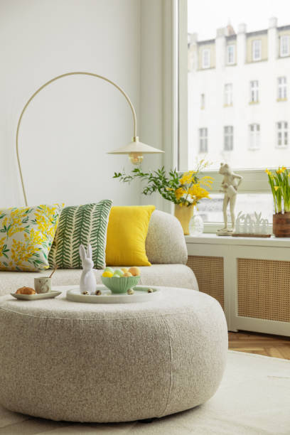 istock Bright living room with an Easter setup featuring yellow tulips in a white vase, soft textured pillows, and delicate decorations, creating a warm and festive ambiance. 2203387902