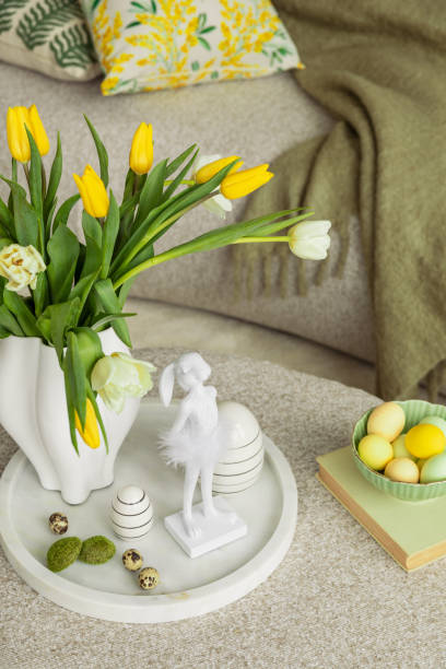 istock Easter table setting in a cozy living space with fresh yellow tulips, a white ceramic vase, and a decorative chicken figurine. A soft color palette and pastel accents create a festive atmosphere. 2203388050