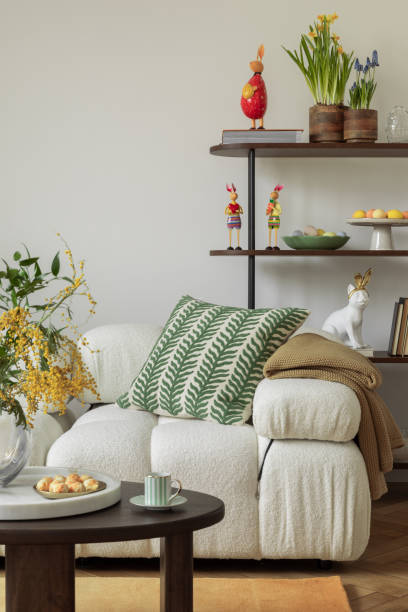 istock A beautifully decorated Easter-themed sofa with textured pillows in green and yellow hues, a soft beige throw, and wooden shelving adorned with festive decorations and spring flowers. 2203388071