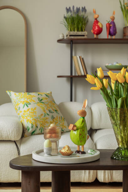 istock Elegant Easter setup with a stone frog sculpture, yellow tulips, and decorative eggs on a wooden side table. 2203388698