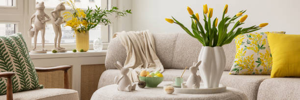 istock Light and airy living space decorated for Easter with soft beige tones, a curved sofa, and a cozy atmosphere. A round ottoman with a marble tray holds pastel eggs, ceramic bunnies, and a cup of coffee. 2203388824