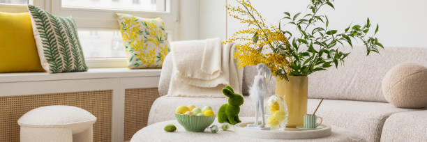 istock Light and airy living space decorated for Easter with soft beige tones, a curved sofa, and a cozy atmosphere. A round ottoman with a marble tray holds pastel eggs, ceramic bunnies, and a cup of coffee. 2203388853