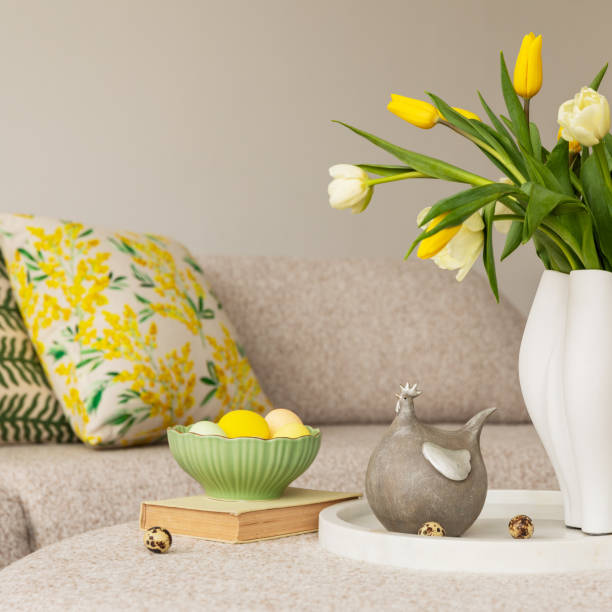 istock Easter table setting in a cozy living space with fresh yellow tulips, a white ceramic vase, and a decorative chicken figurine. A soft color palette and pastel accents create a festive atmosphere. 2203388861