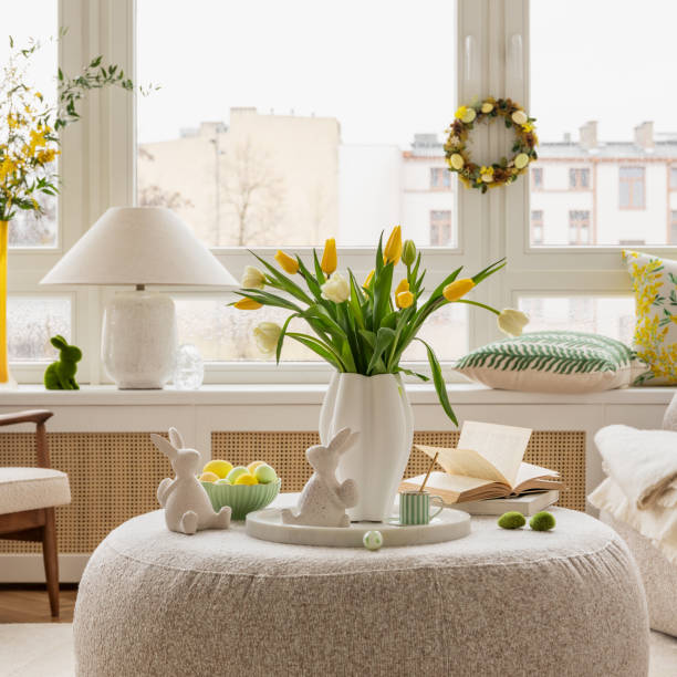istock Light and airy living space decorated for Easter with soft beige tones, a curved sofa, and a cozy atmosphere. A round ottoman with a marble tray holds pastel eggs, ceramic bunnies, and a cup of coffee. 2203388970