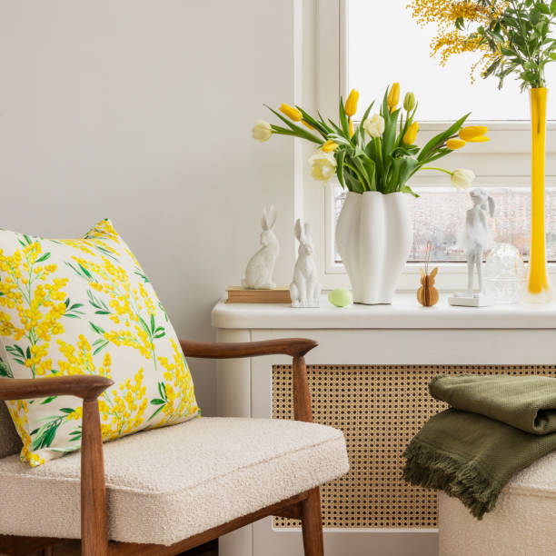 istock Light and airy living space decorated for Easter with soft beige tones, a curved sofa, and a cozy atmosphere. A round ottoman with a marble tray holds pastel eggs, ceramic bunnies, and a cup of coffee. 2203388975