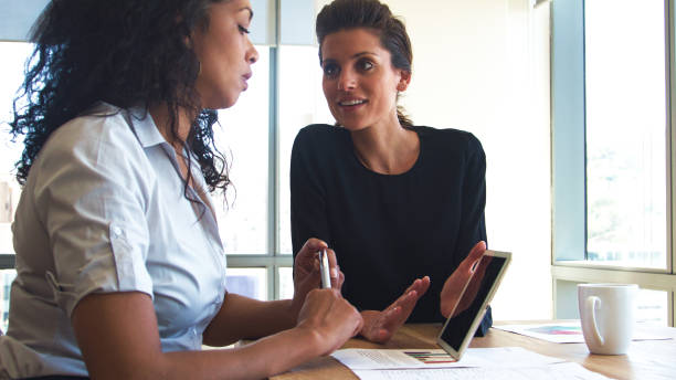 istock Two Female Business Colleagues Sitting At Desk In Office Working At Laptop Together 2203390708