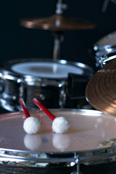 Timpani mallets are lying on a kettledrum in a recording studio, drums in the background.