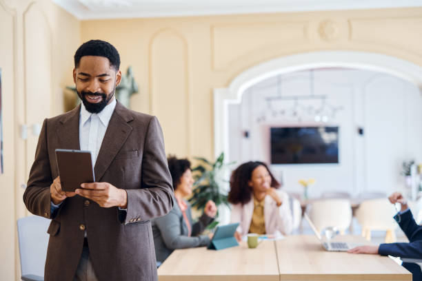 istock Smiling businessman using digital tablet in modern office with colleagues working in background 2203400537