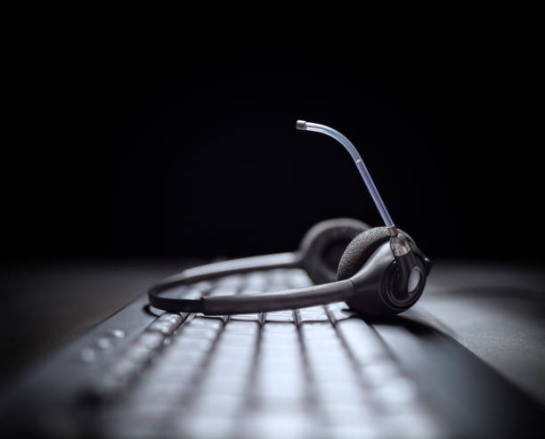 istock Headset headphones telephone with microphone on computer keyboard in support and customer service help desk call center dark background 2203401420