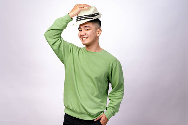 istock An Asian man in a green sweater is playfully holding a fedora hat above his head while smiling. He looks cheerful and stylish against a plain white background 2203401934