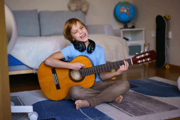 istock Boy singing and playing guitar at home 2203402353