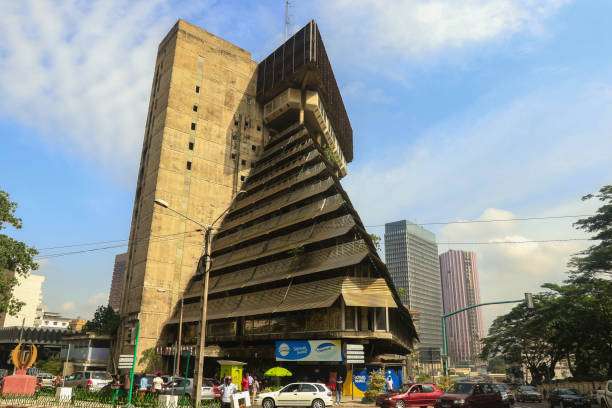 Unique architectural design of a building in Abidjan, Ivory Coast showcasing modern urban life Abidjan, Ivory Coast - November 16, 2024: A striking building in Abidjan features an unusual triangular shape, surrounded by bustling city streets and vehicles under a clear sky. abidjan skyline stock pictures, royalty-free photos & images