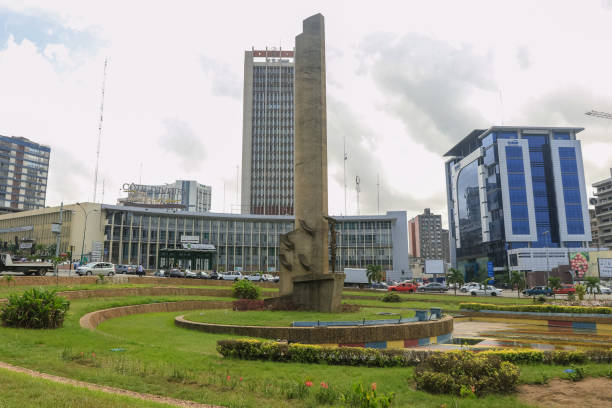 Abidjan, Ivory Coast - November 16, 2024: Tall monument surrounded by greenery and cityscape in Abidjan, illustrating the vibrant culture and modernity of the area.