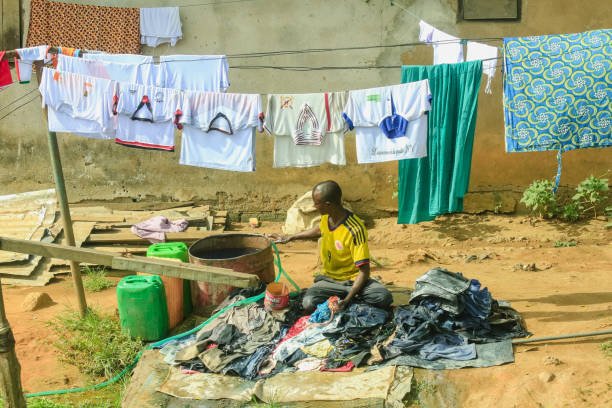 Abidjan, Ivory Coast - November 16, 2024: A man washes clothes in a basin beside drying garments suspended on a line in Abidjan. The activity reflects daily life in the city.