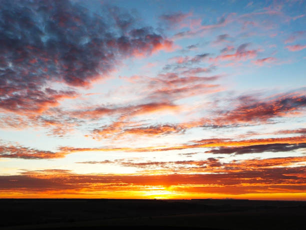 A mesmerizing sunrise paints the sky with vibrant shades of orange, yellow, and red, casting a warm glow over the scattered clouds. This picturesque scene captures the serene beauty of nature, perfect for showcasing dramatic landscapes and atmospheric photography.