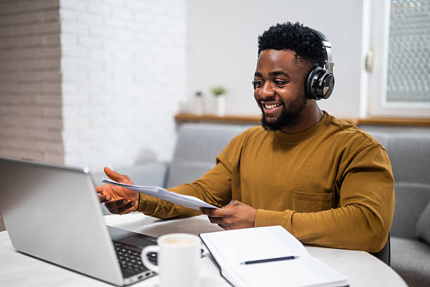 Young African entrepreneur with headphones using laptop while attending video call at home