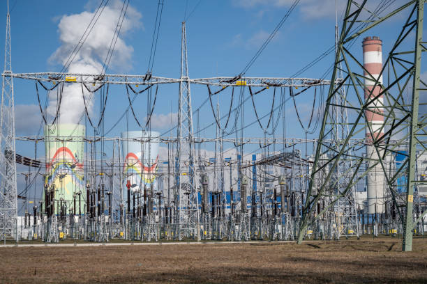 Image of a power plant at sunrise, featuring two large industrial chimneys emitting smoke into the clear blue sky. This photo is ideal for use in topics related to energy production, environmental impact, and industrial landscapes