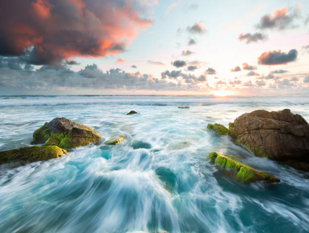 Stormy water rushing around rocks, moss and sunset
