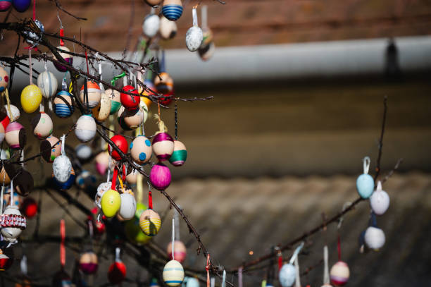 A detailed close-up of brightly colored Easter eggs hanging from a tree branch, illuminated by sunlight. The festive decorations, featuring various shades and patterns, create a joyful and vibrant atmosphere. The blurred background enhances the depth, making the eggs stand out beautifully.