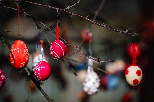 A detailed close-up of brightly colored Easter eggs hanging from a tree branch, illuminated by sunlight. The festive decorations, featuring various shades and patterns, create a joyful and vibrant atmosphere. The blurred background enhances the depth, making the eggs stand out beautifully.