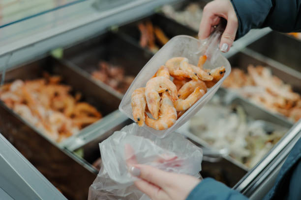 Young woman customer choosing fresh raw shrimp from assortment of fish store