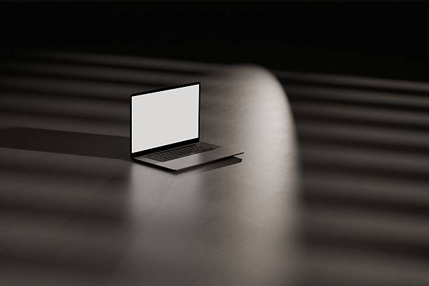 A closeup shot of a half-open laptop shining light on a dark table
