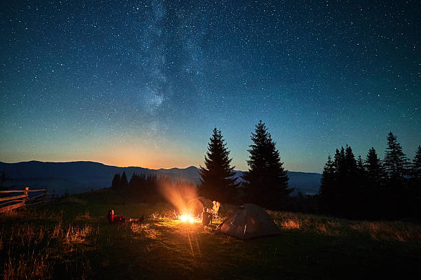istock Group of hikers resting around campfire, surrounded by illuminated tents under stunning starry sky. 2203425324