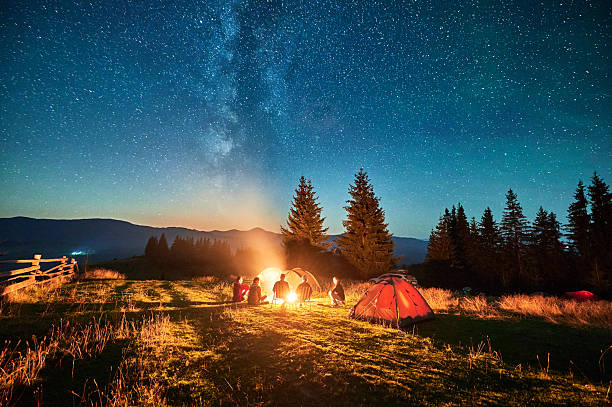 istock Group of hikers resting around campfire, surrounded by illuminated tents under stunning starry sky. 2203425335