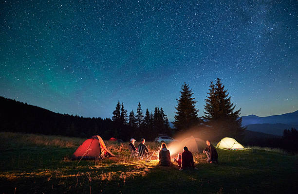 istock Group of hikers resting around campfire, surrounded by illuminated tents under stunning starry sky. 2203425339