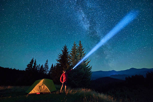 istock Man hiker stands under dazzling starry sky, shining flashlight into heavens. 2203425362