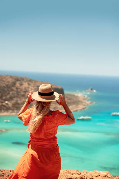 Woman standing on a cliff edge overlooking serene ocean. Copy space. Vertical image