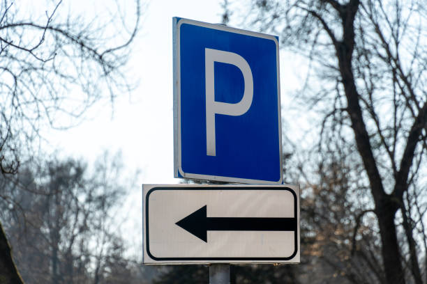 istock A blue parking sign stands tall next to a directional sign pointing left, surrounded by bare trees in a park setting on a sunny day 2203428683