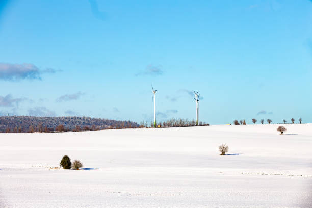 Footprints lead across a vast snowy plateau toward two wind turbines under a pale winter sky in northern Norway, symbolizing clean energy and remote exploration.