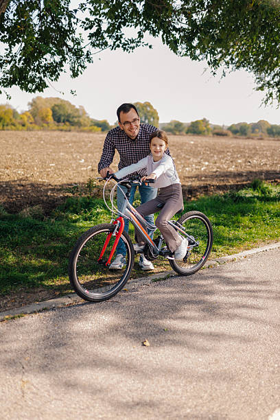 Father teaching his daughter how to ride a bicycle on a sunny day in the countryside