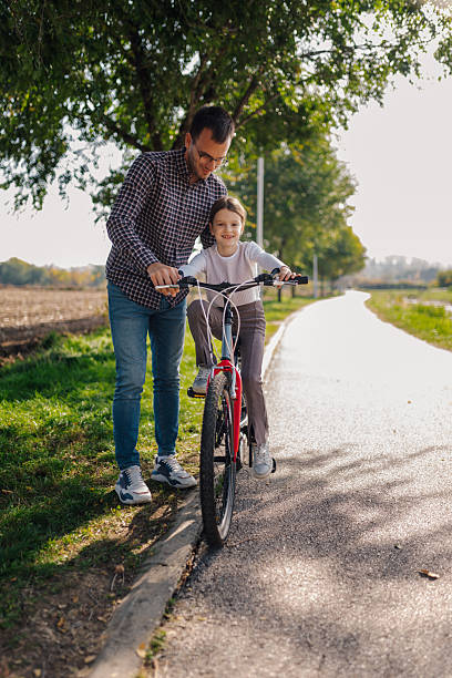 Father teaching daughter riding bicycle in a park during summer vacation