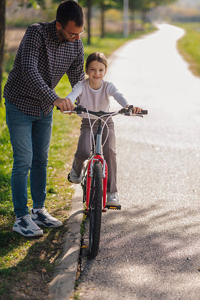 istock Father teaching daughter riding bicycle in park 2203437716