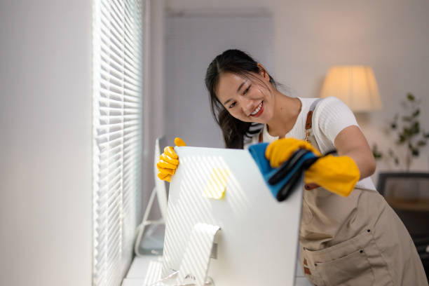 istock Young Asian woman sanitizing computer monitor while wearing protective gloves, maintaining clean home office workspace 2203438134