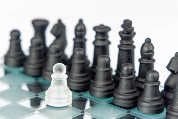istock A single white pawn stands against black chess pieces on a mirrored chessboard, conveying deep strategic thinking and perseverance 2203443777
