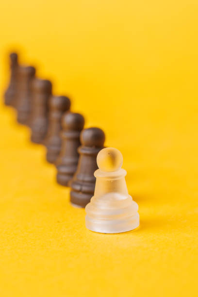 A single white pawn among black ones on a yellow background creates a strong metaphor for diversity, individuality, and breaking societal norms