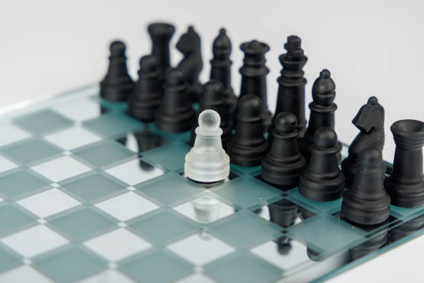 Black chess pieces lined up against a single white pawn on a mirrored chessboard, creating a dramatic strategy concept on a white background