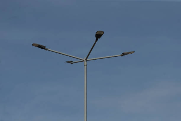A tall street light pole equipped with three bright lights mounted on it, set against a beautiful clear blue sky backdrop