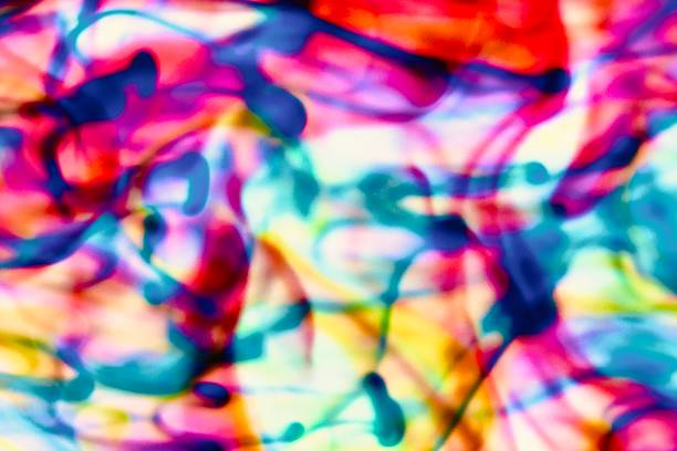 Abstract blur focus vibrant colors flowing with colored inks dispersed in water. The composition consists of shades of blue, red, green and yellow blending and swirling on a light background, creating