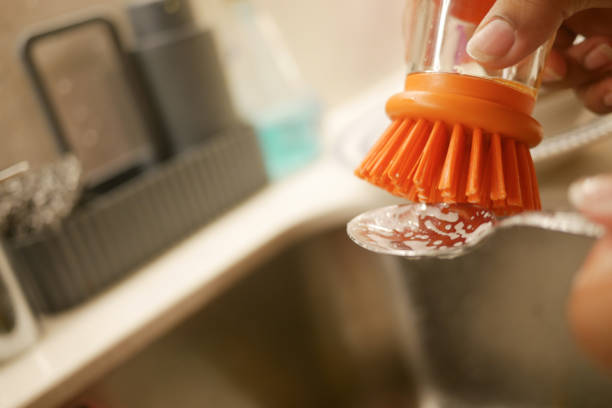 In the kitchen sink, a glass is being thoroughly cleaned using a brush along with soap
