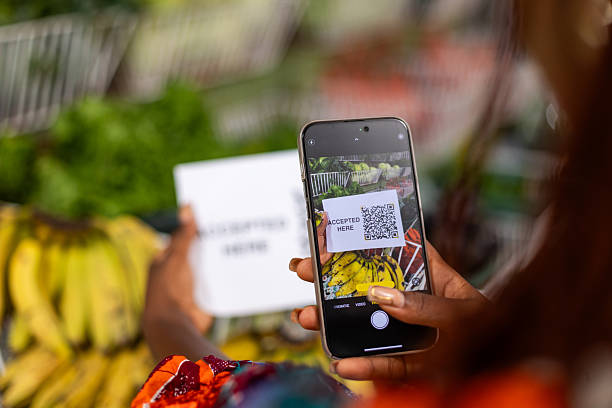 istock Close-up shot of a person's hand using a smartphone to scan a QR Code for contactless payment at a fruits and vegetables shop where other groceries are also sold. 2203465434