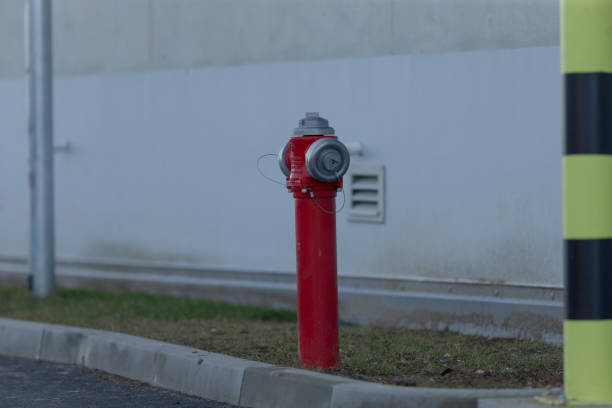 A bright red fire hydrant is positioned right next to a tall yellow pole that stands out against its surroundings on the sidewalk